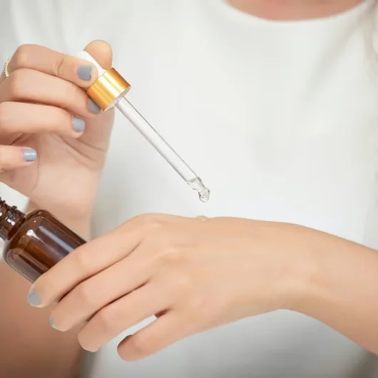 Hand holding the serum dropper above the back of the other hand, dispensing one drop