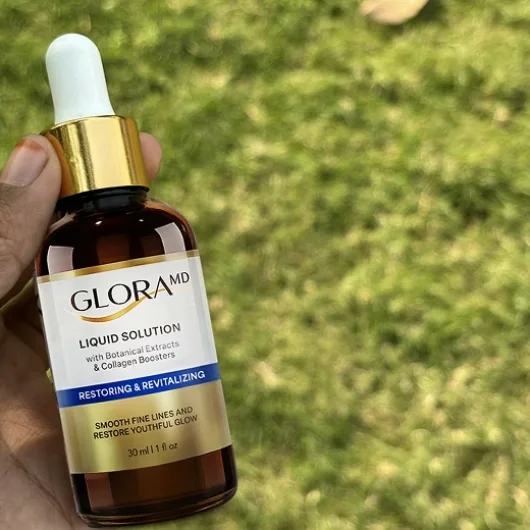 A hand holding the GloraMD bottle outdoors over grass, the label legible